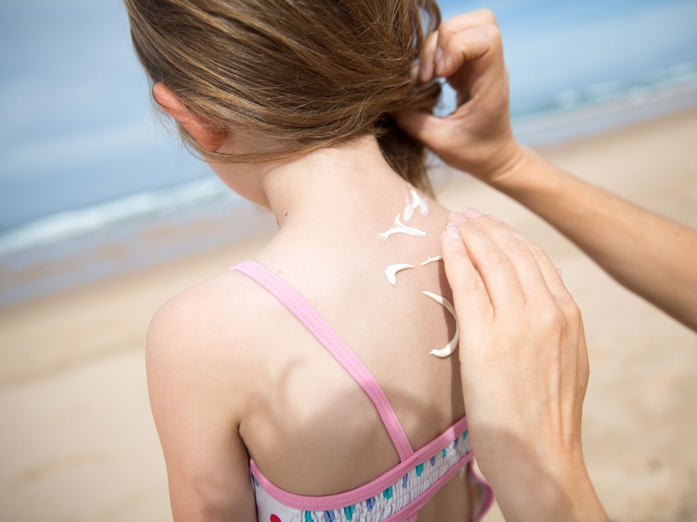 Eine Frau cremt ihre Tochter mit Sonnencreme ein