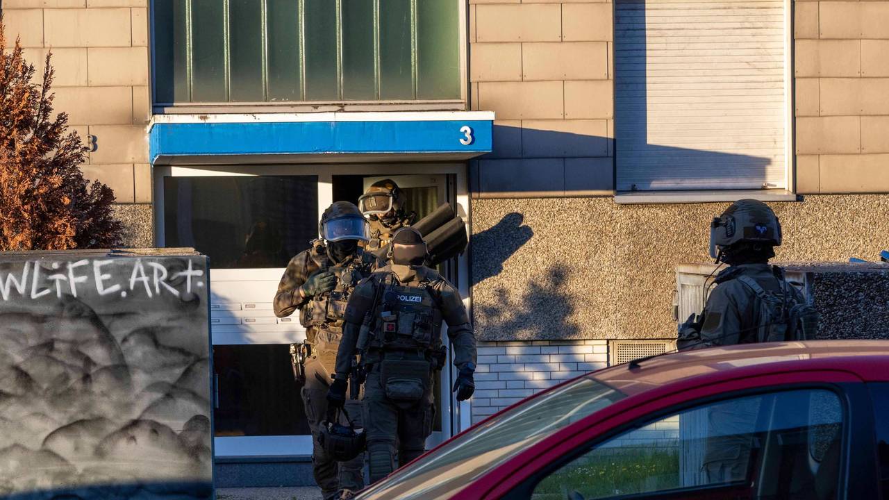 Vermummte Spezialkräfte in Tarnkleidung verlassen ein Haus.