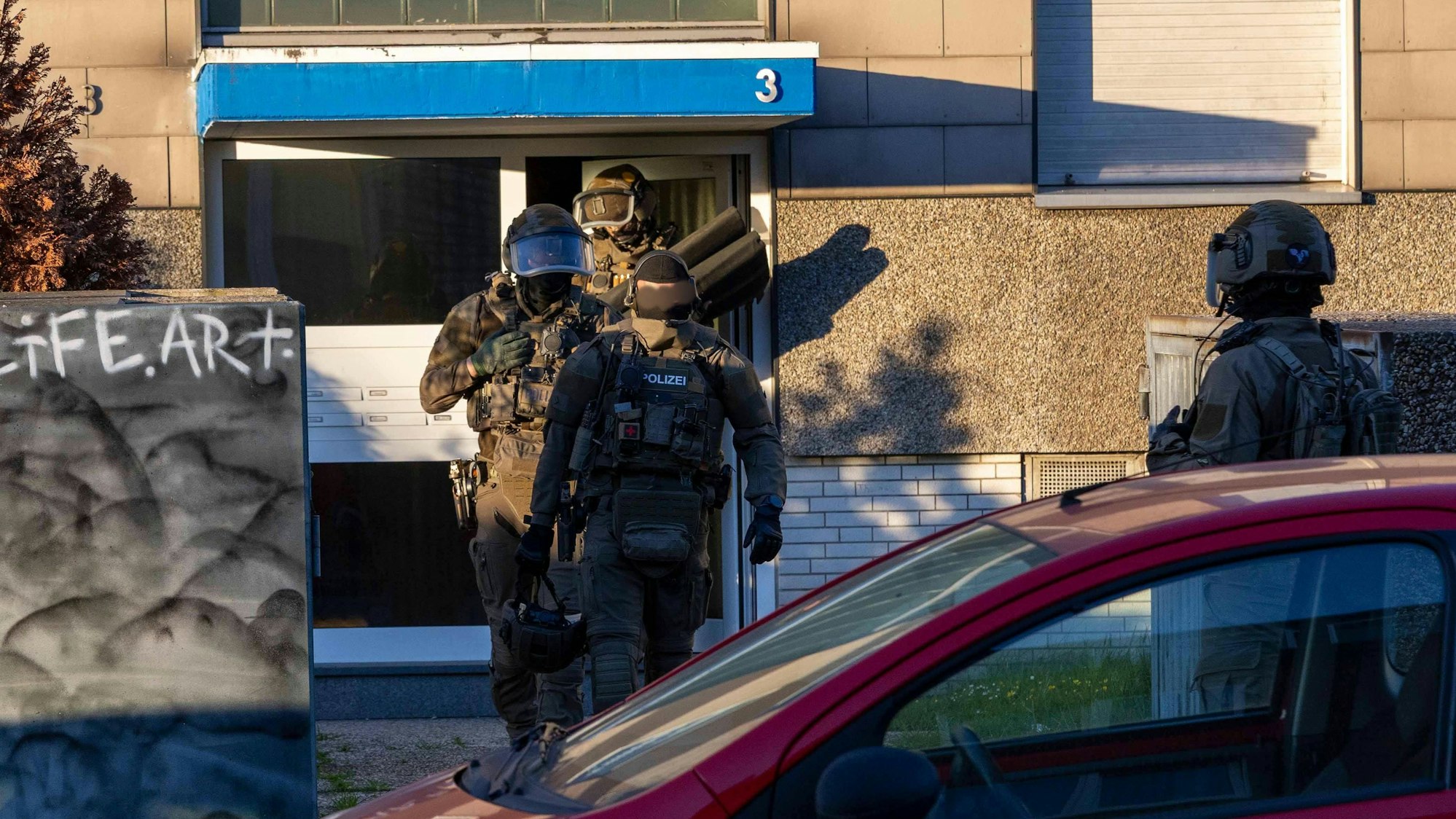 Vermummte Spezialkräfte in Tarnkleidung verlassen ein Haus.
