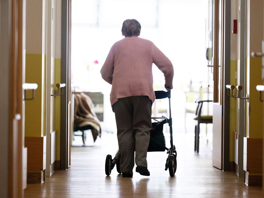 Eine Frau geht mit einem Rollator in einem Altenheim