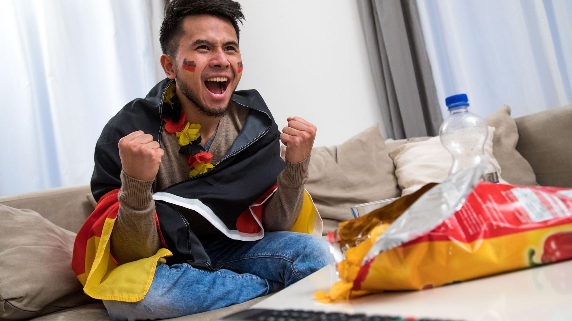 Ein Mann fiebert in WM-Deko vor dem Fernseher mit
