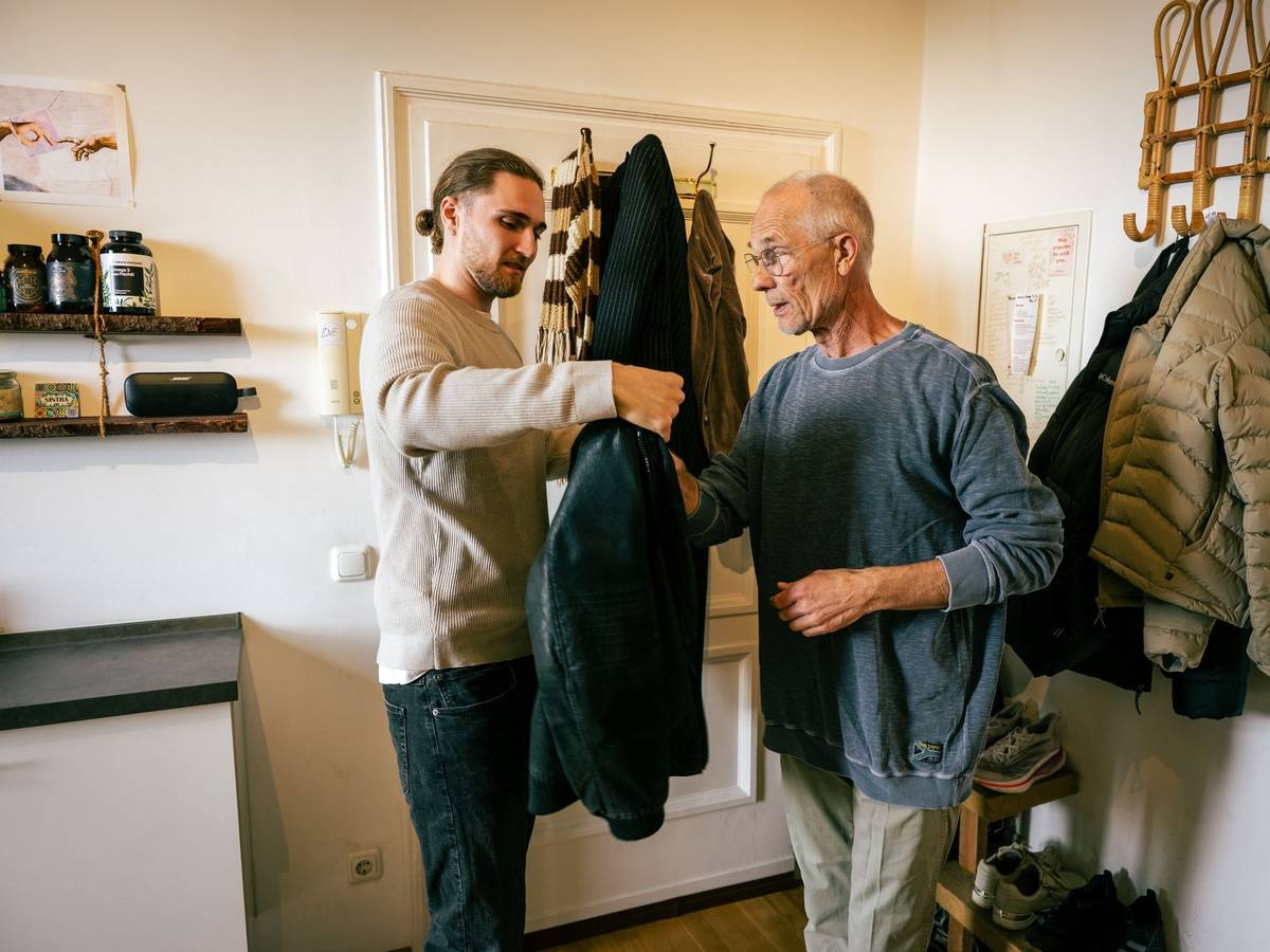 Ein junger Mann hilft einem Senior die Jacke anzuziehen