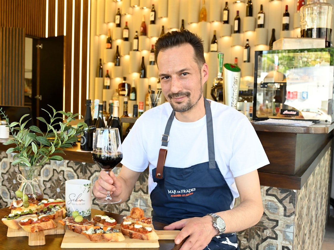 Ein Mann mit Wein in der Hand schaut in die Kamera.