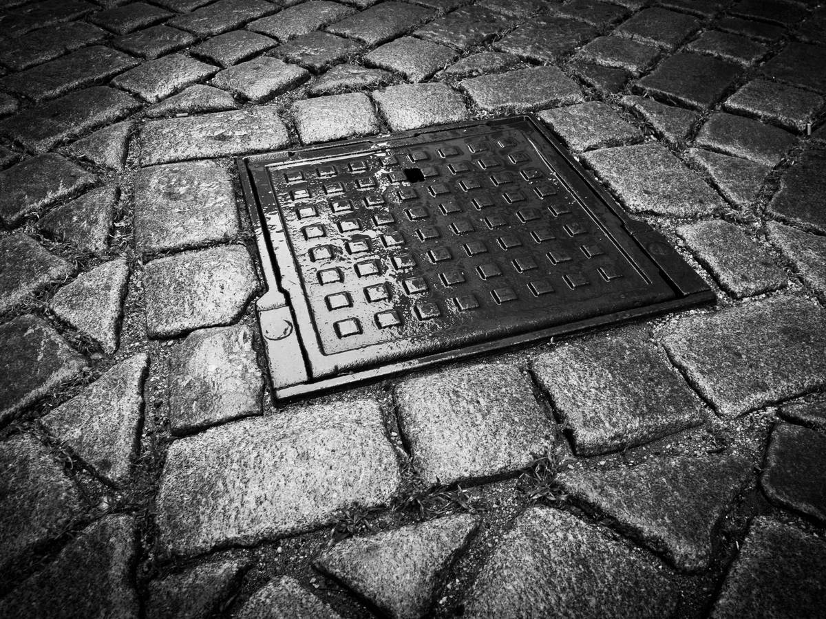 Dunkler Gullydeckel auf Kopfsteinpflaster
