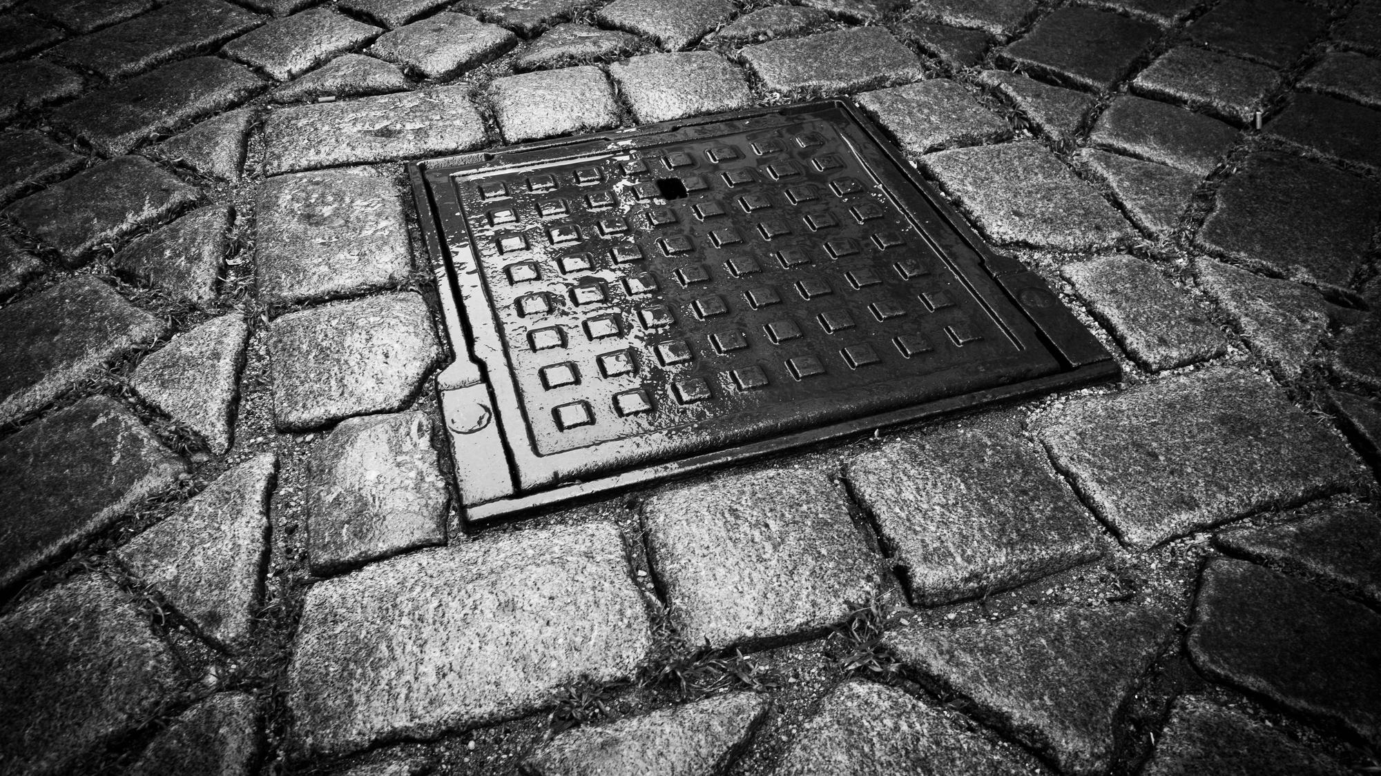 Dunkler Gullydeckel auf Kopfsteinpflaster