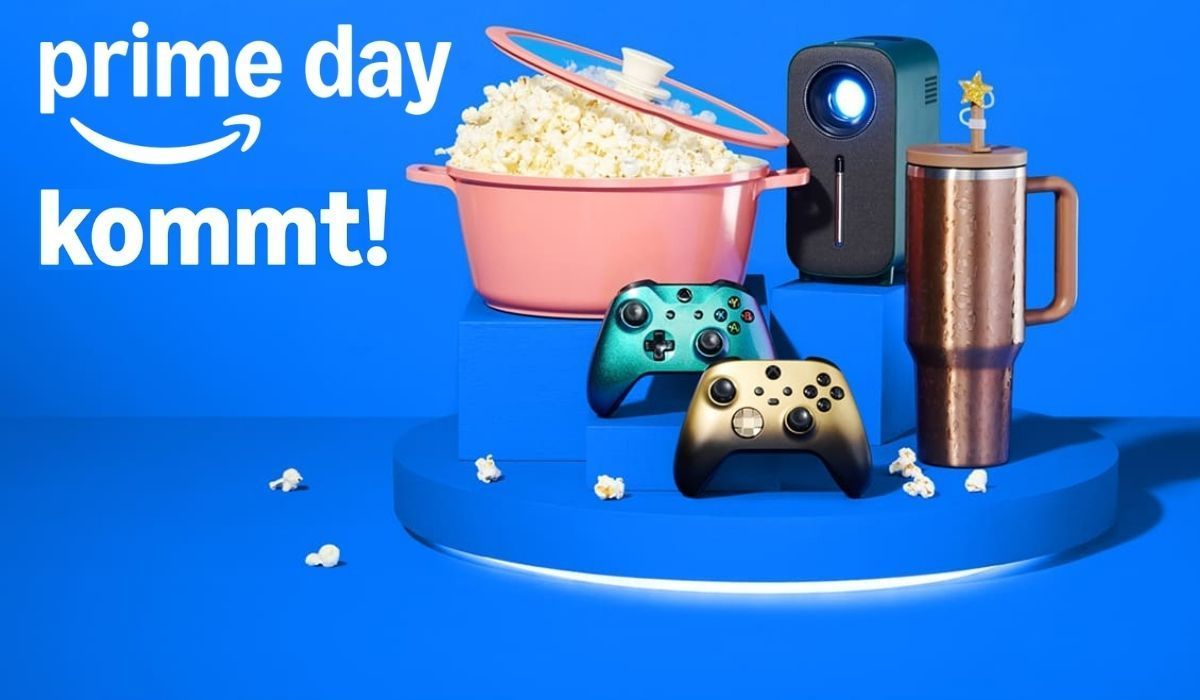 Ankündigungsbild zum Amazon Prime Day 2026 auf blauem Hintergrund mit dem Amazon-Logo und dem Schriftzug "prime day kommt!". Im Vordergrund sind verschiedene Produkte arrangiert: ein rosafarbener Kochtopf gefüllt mit Popcorn, ein kompakter Beamer, zwei Xbox-Controller in Gold und Grün-Metallic sowie ein kupferfarbener Thermobecher.