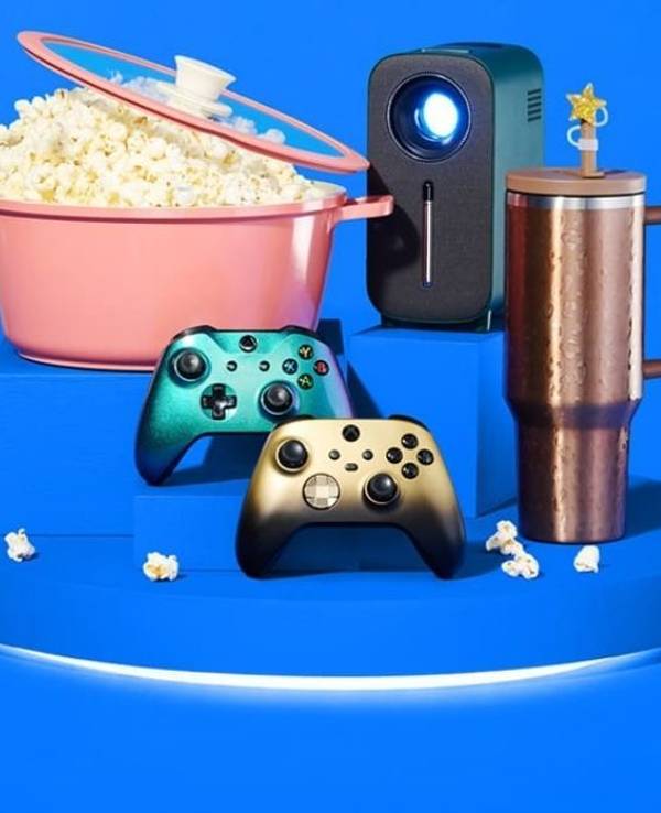 Ankündigungsbild zum Amazon Prime Day 2026 auf blauem Hintergrund mit dem Amazon-Logo und dem Schriftzug "prime day kommt!". Im Vordergrund sind verschiedene Produkte arrangiert: ein rosafarbener Kochtopf gefüllt mit Popcorn, ein kompakter Beamer, zwei Xbox-Controller in Gold und Grün-Metallic sowie ein kupferfarbener Thermobecher.