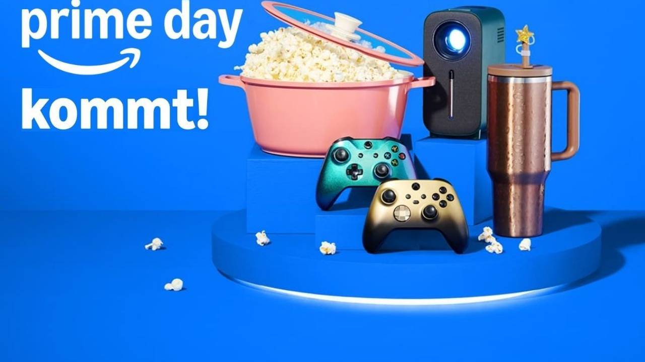 Ankündigungsbild zum Amazon Prime Day 2026 auf blauem Hintergrund mit dem Amazon-Logo und dem Schriftzug "prime day kommt!". Im Vordergrund sind verschiedene Produkte arrangiert: ein rosafarbener Kochtopf gefüllt mit Popcorn, ein kompakter Beamer, zwei Xbox-Controller in Gold und Grün-Metallic sowie ein kupferfarbener Thermobecher.