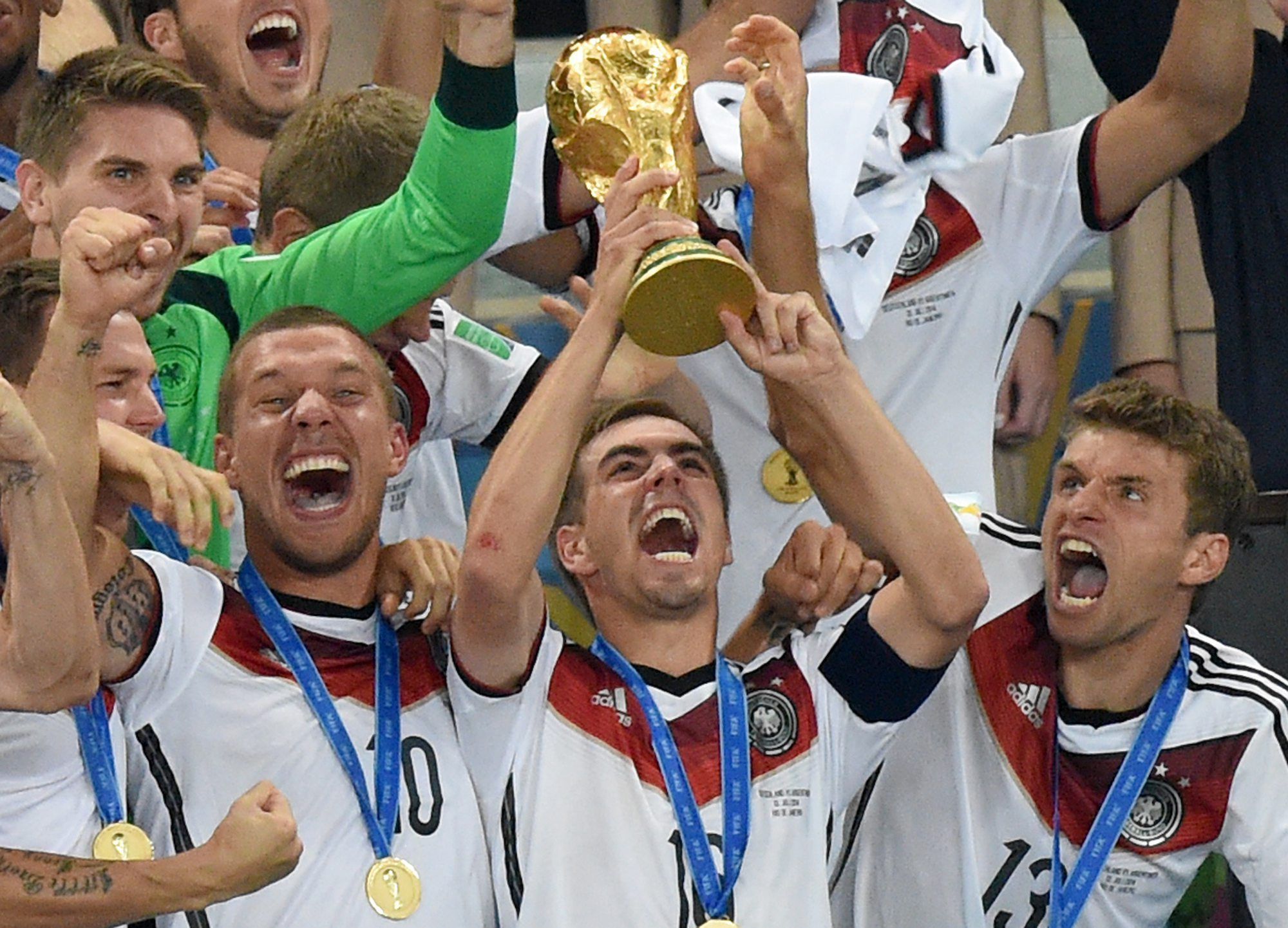 Philipp Lahm (M) jubelt mit dem WM-Pokal zwischen seinen Teamkollegen Lukas Podolski (l) und Thomas Müller (r) während der Siegerehrung auf der Tribüne nach dem Finalsieg gegen Argentinien im Estadio do Maracana.