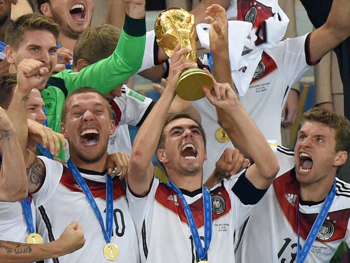 Philipp Lahm (M) jubelt mit dem WM-Pokal zwischen seinen Teamkollegen Lukas Podolski (l) und Thomas Müller (r) während der Siegerehrung auf der Tribüne nach dem Finalsieg gegen Argentinien im Estadio do Maracana.