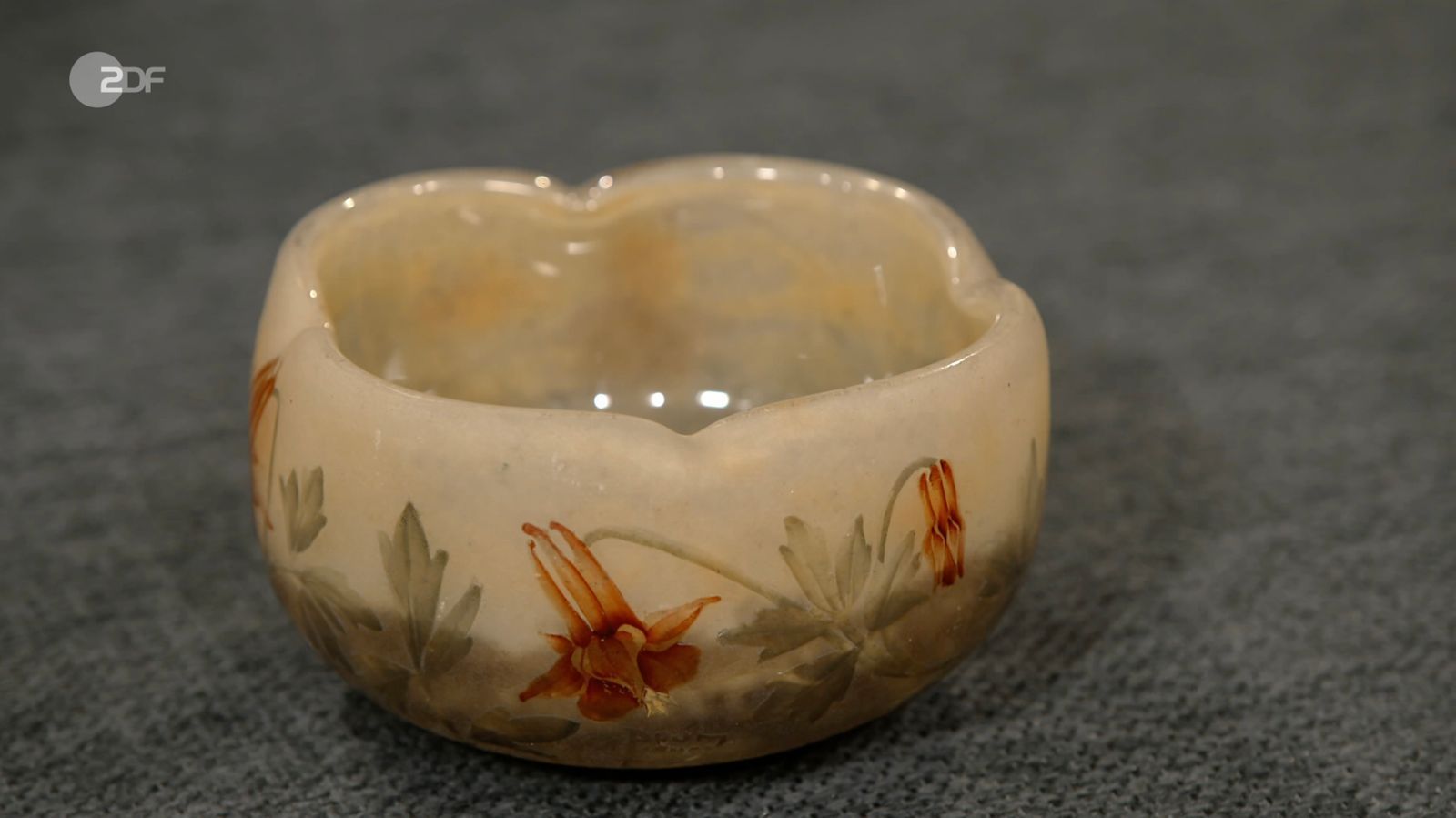 Das besondere Farbspiel der Schale entstand, indem bei der Herstellung farbiges Pulver in das farblose Glas eingestreut wurde, erläuterte Berding die Patinage. Bemalt mit Emaille wurde das Stück mit Akelei-Blüten, ein Symbol für Liebe und Fruchtbarkeit. „Das ist handwerklich äußerst gut gemacht“, schwärmte die Expertin. (Bild: ZDF)