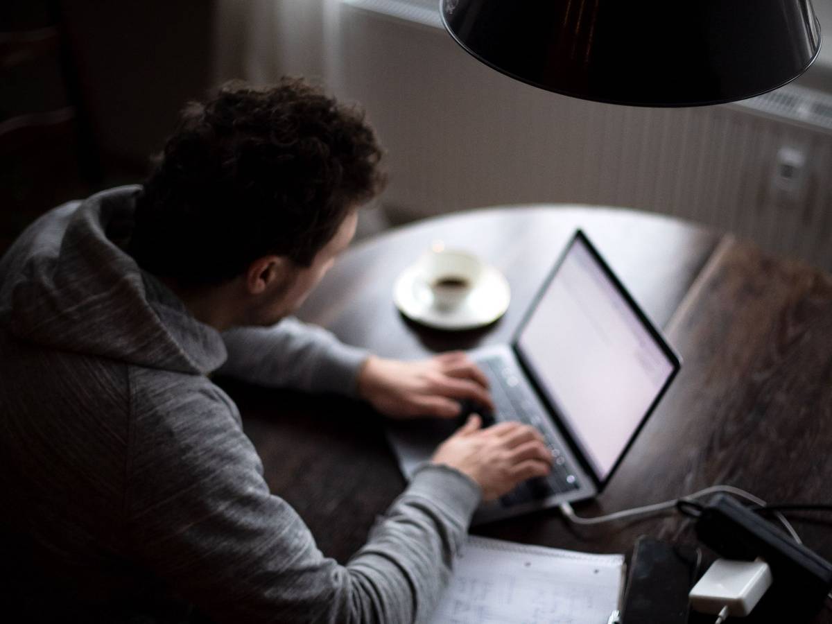Ein Mann sitzt mit Laptop am Küchentisch
