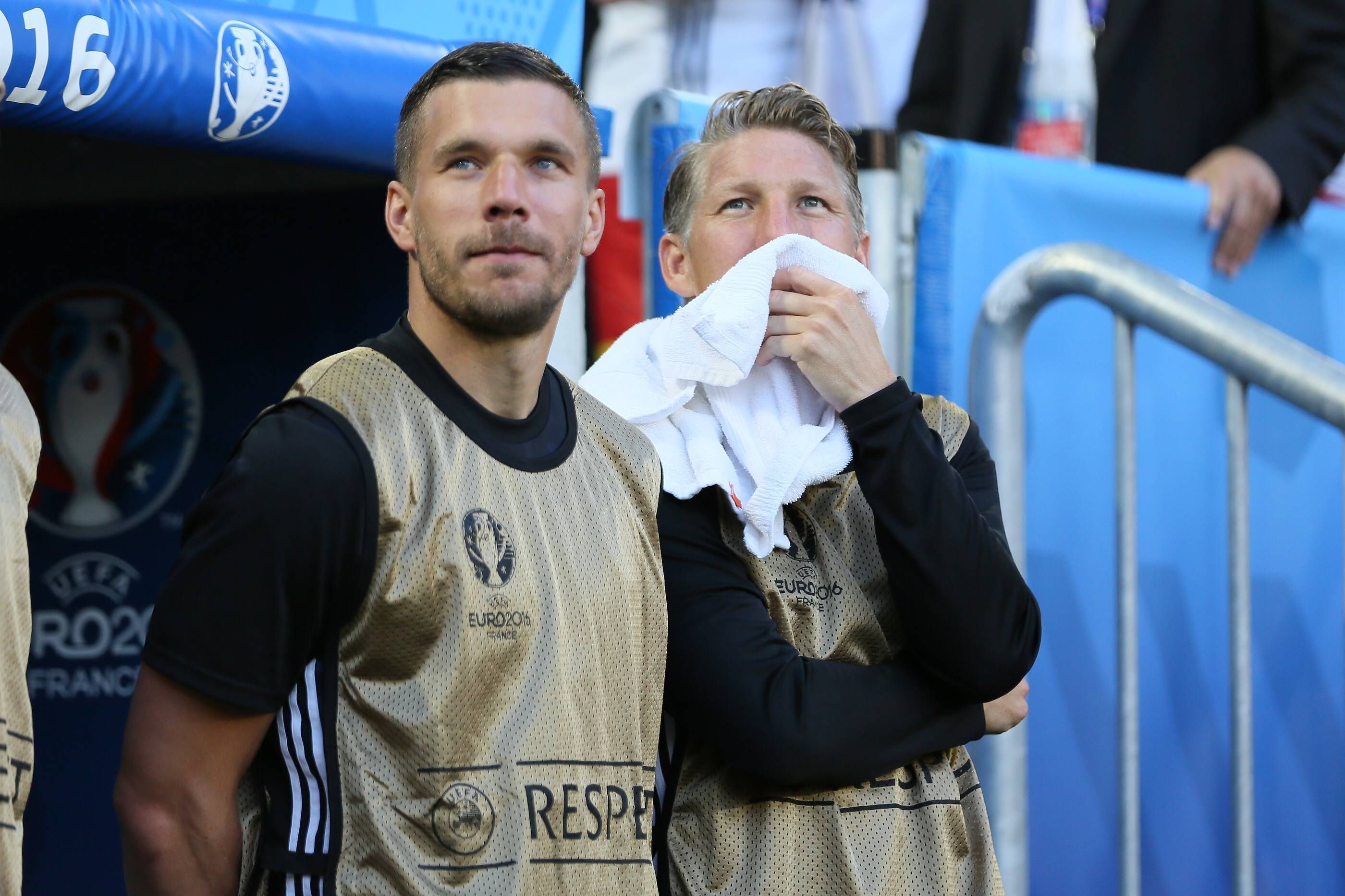 Lukas Podolski und Bastian Schweinsteiger stehen als Ersatzspieler vor der Bank.