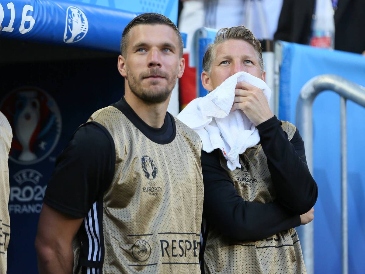 Lukas Podolski und Bastian Schweinsteiger stehen als Ersatzspieler vor der Bank.