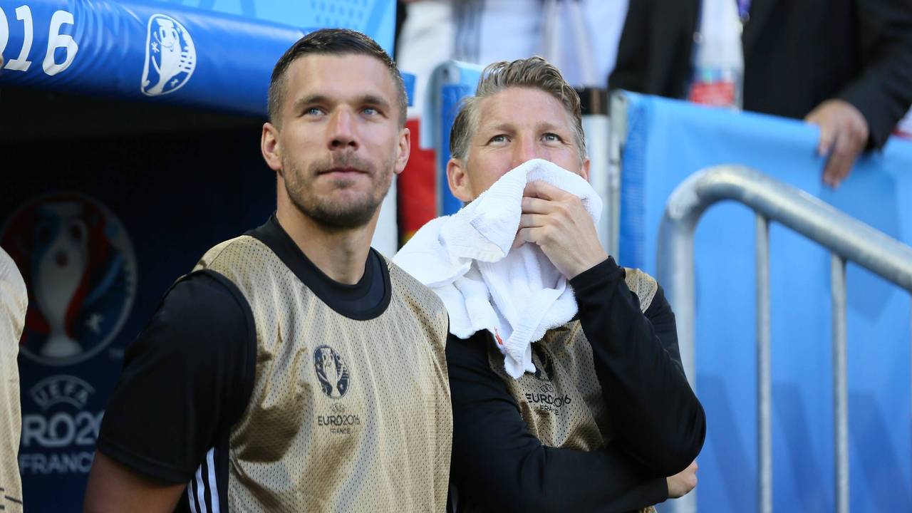 Lukas Podolski und Bastian Schweinsteiger stehen als Ersatzspieler vor der Bank.