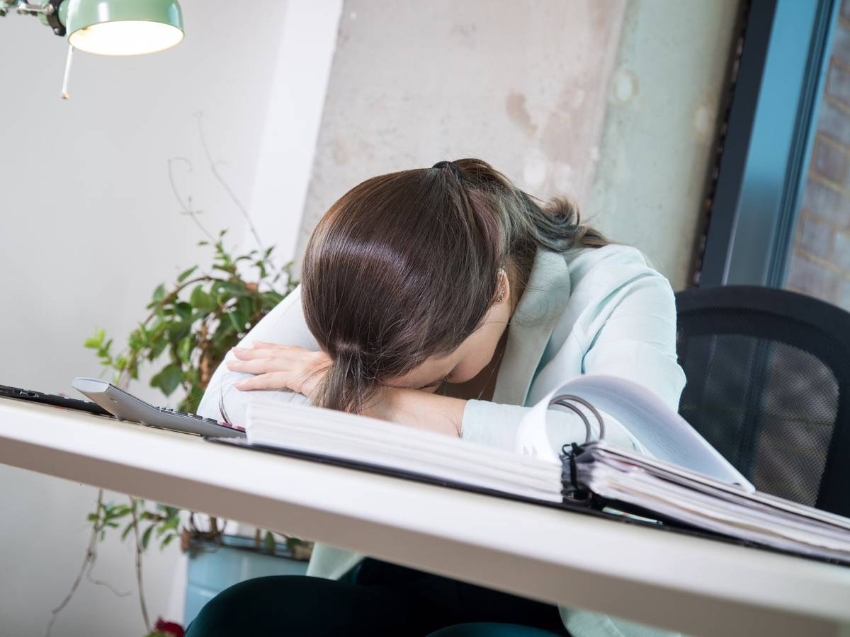 Eine Frau legt ihren Kopf erschöpft auf den Schreibtisch