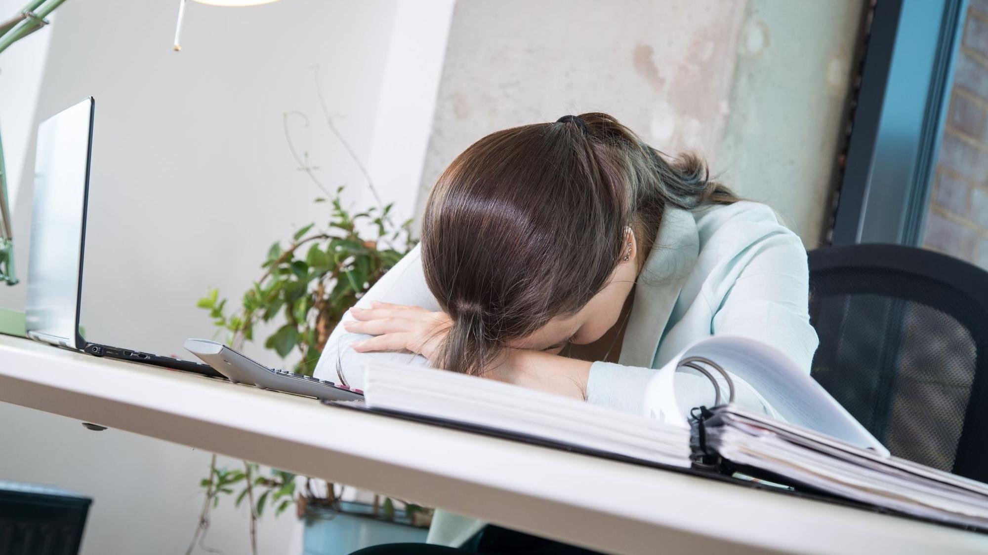 Eine Frau legt ihren Kopf erschöpft auf den Schreibtisch