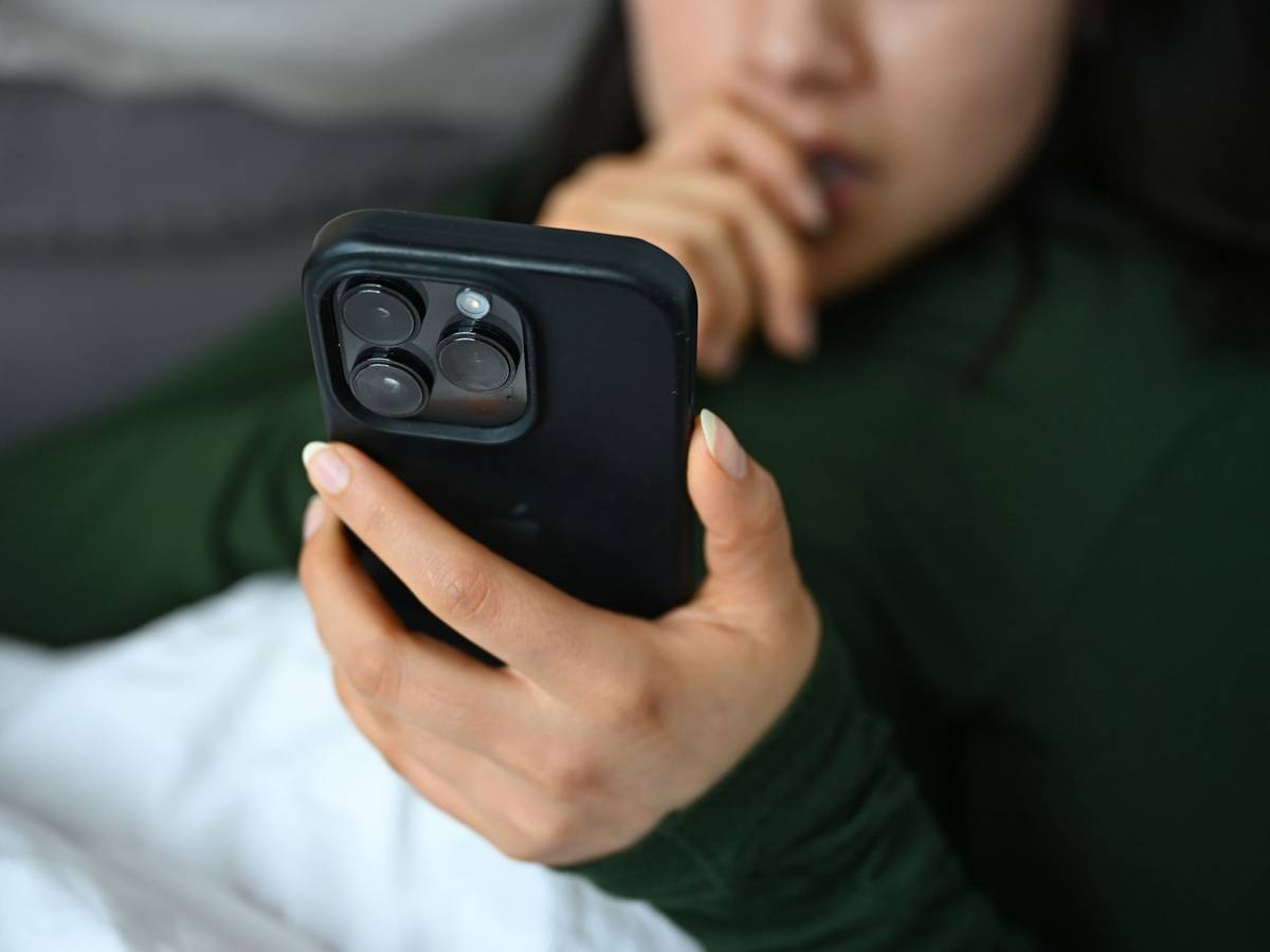 Eine junge Frau liegt mit ihrem Handy auf der Couch