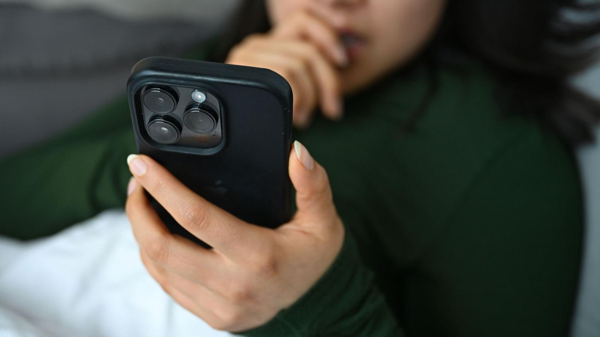 Eine junge Frau liegt mit ihrem Handy auf der Couch