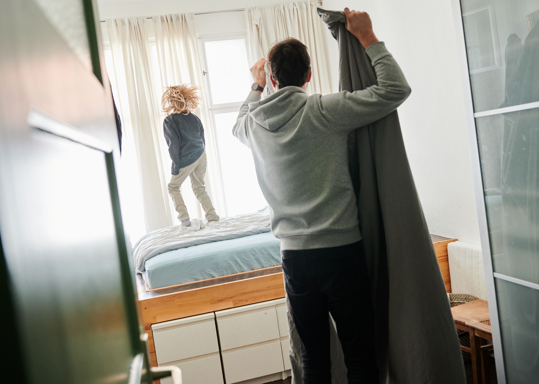 Ein Mann bezieht ein Bett während ein Kind auf dem Bett hüpft