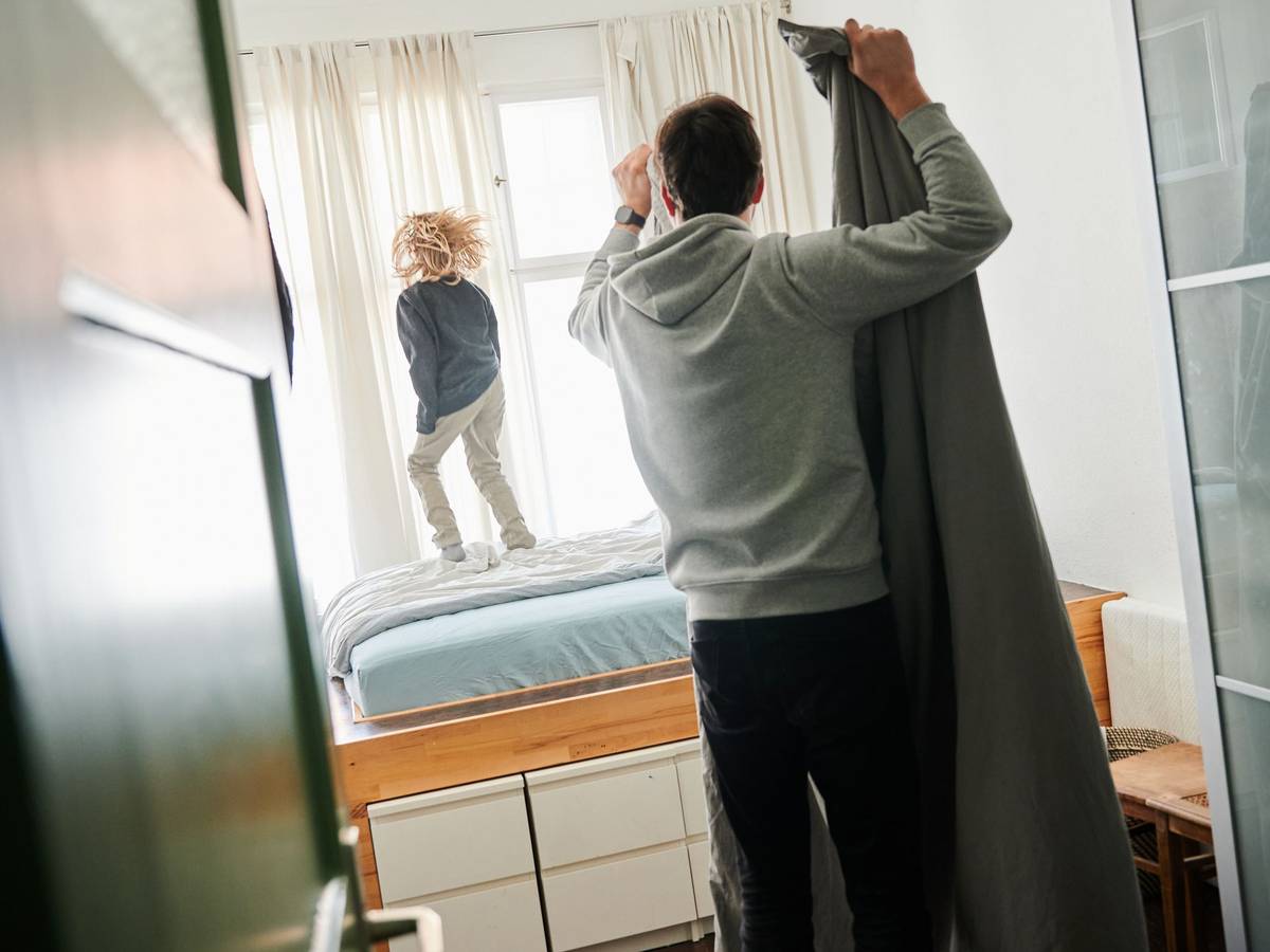 Ein Mann bezieht ein Bett während ein Kind auf dem Bett hüpft