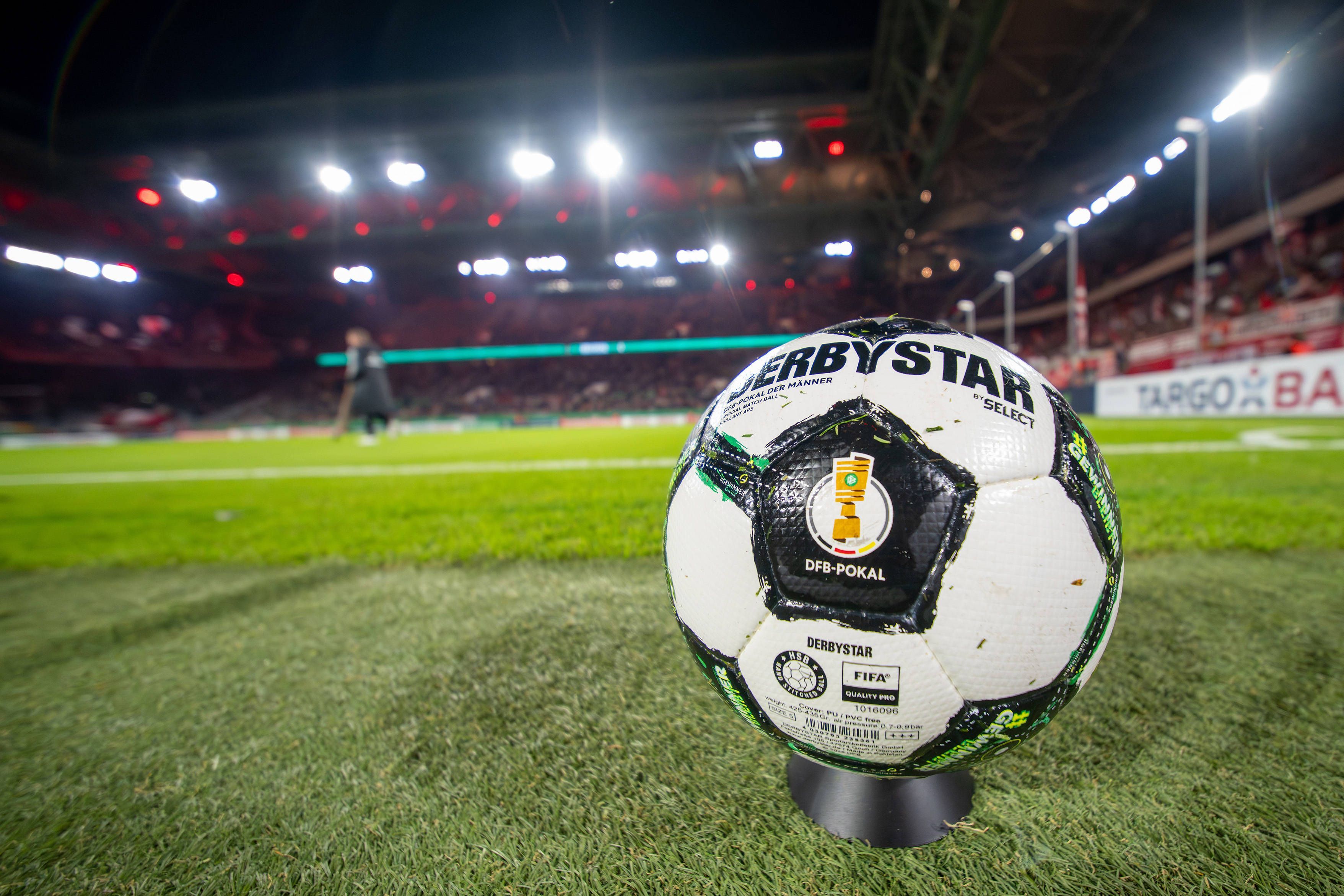 Ein Derbystar-Ball des DFB-Pokals liegt auf dem Rasen. Im Hintergrund sieht man das Stadion von Fortuna Düsseldorf.