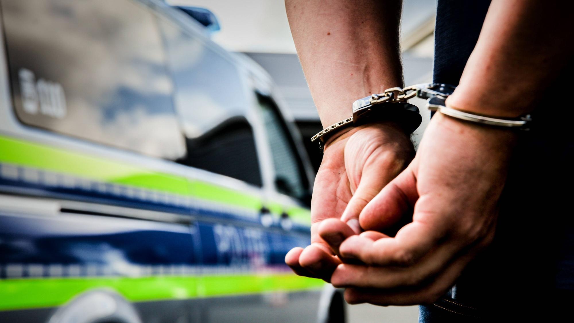 Mann in Handschellen vor Polizeiwagen