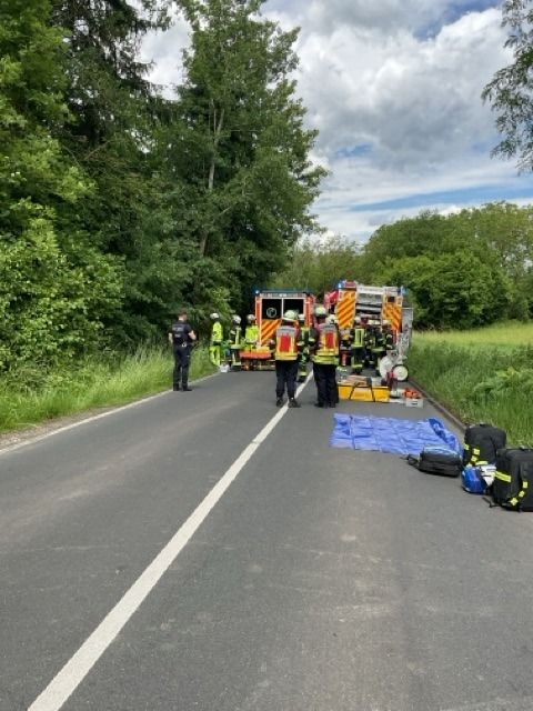 Ein verunfalltes Auto steht am Straßenrand, umgeben von Feuerwehrleuten.