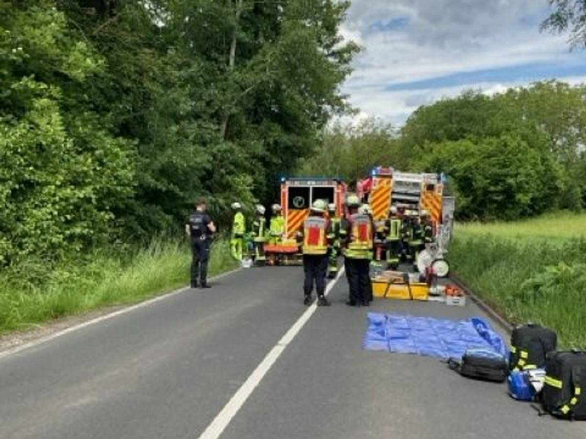 Ein verunfalltes Auto steht am Straßenrand, umgeben von Feuerwehrleuten.