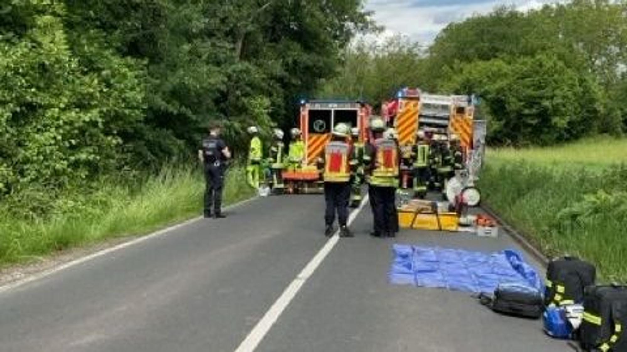 Ein verunfalltes Auto steht am Straßenrand, umgeben von Feuerwehrleuten.