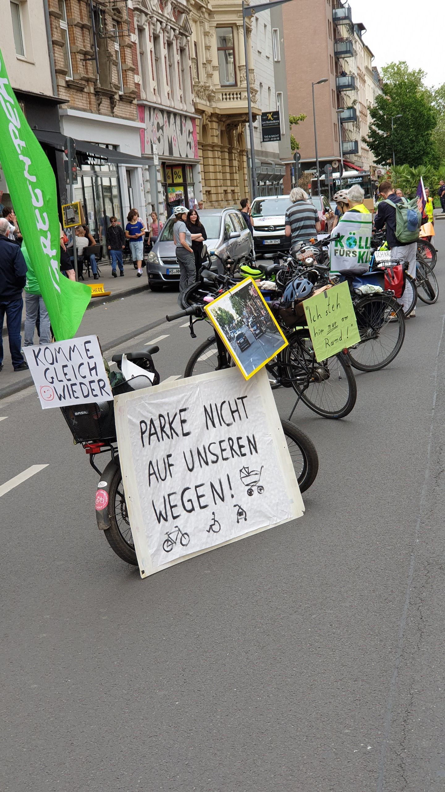 Fahrräder stehen auf der Fahrbahn, an ihnen hängen Plakate u. a. mit der Aufschrift: Parke nicht auf unseren Wegen!