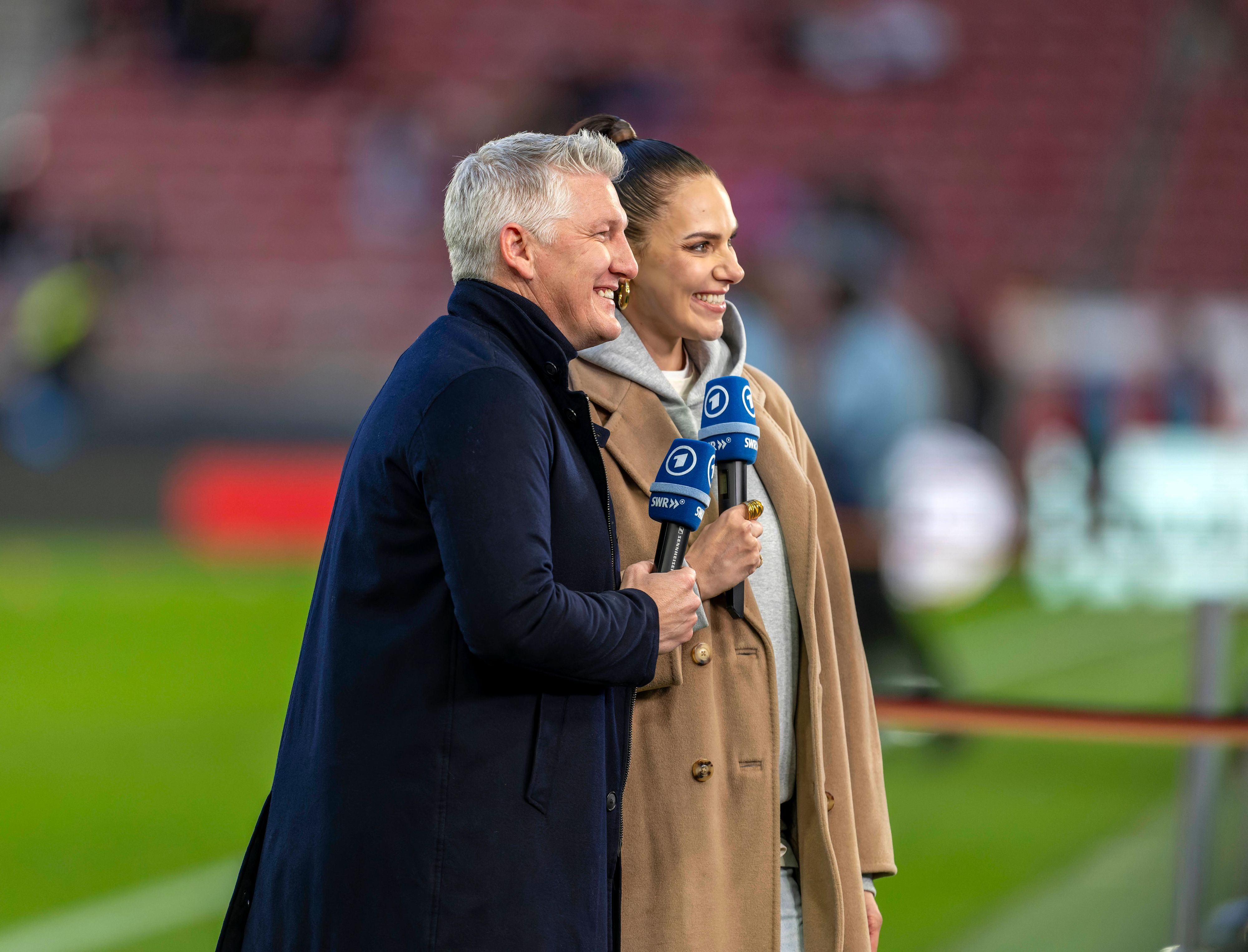 Bastian Schweinsteiger und Esther Sedlaczek mit Mikrofonen lächelnd.