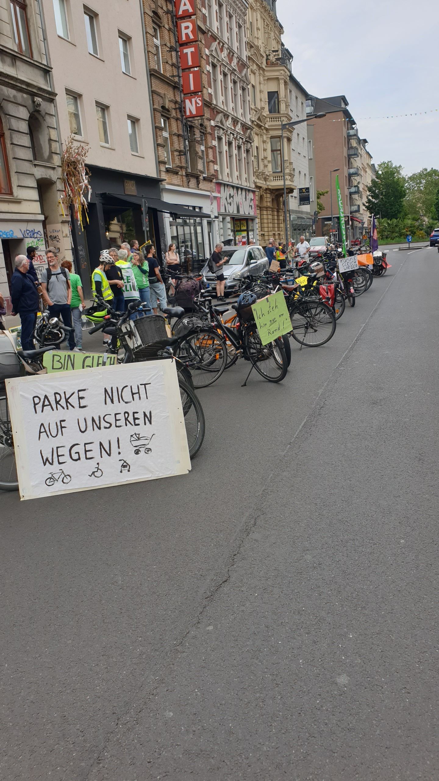 Fahrräder stehen auf der Fahrbahn, an ihnen hängen Plakate u. a. mit der Aufschrift: Parke nicht auf unseren Wegen!