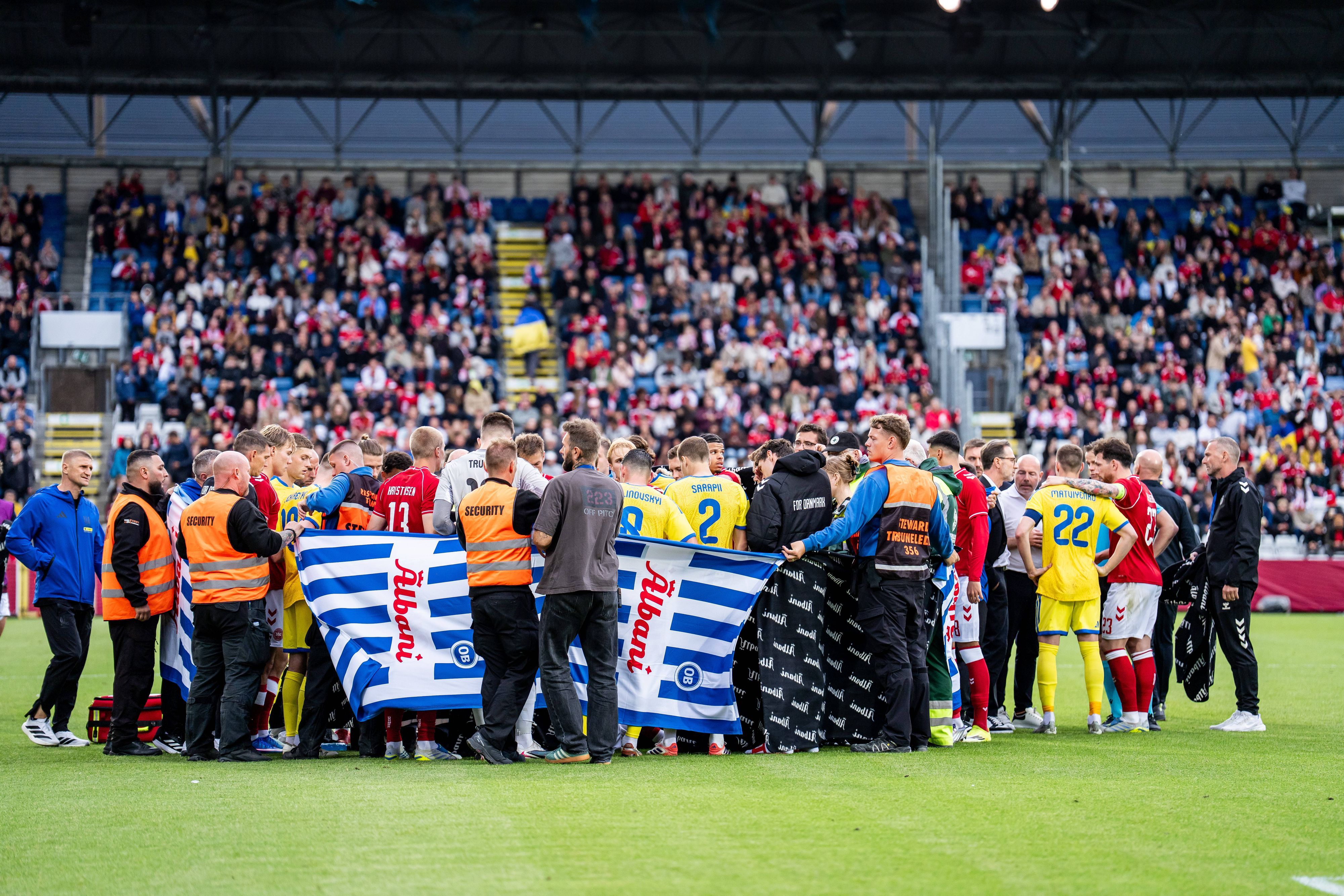 Dänische und ukrainische Spieler versammeln sich nach dem Zusammenbruch des dänischen Spielers Christian Eriksen auf dem Spielfeld.