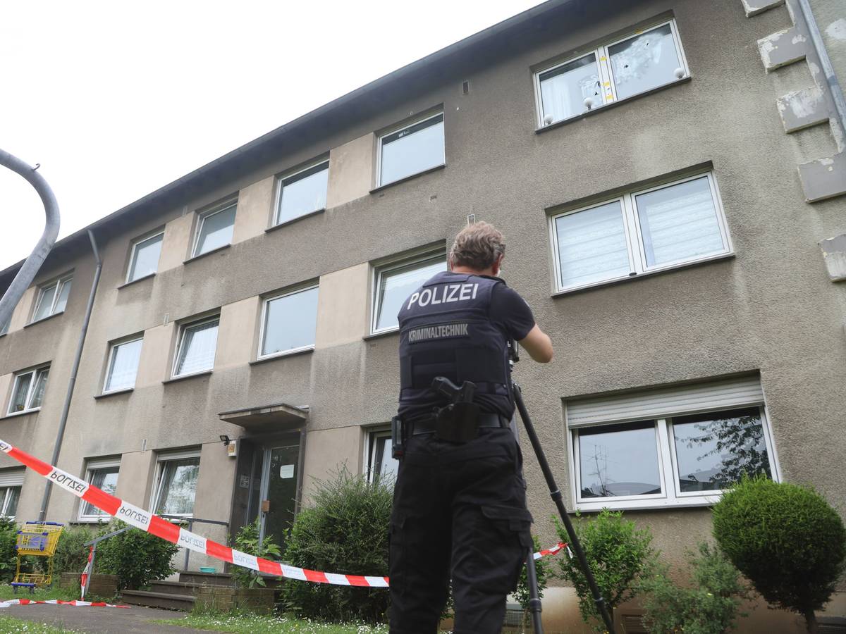 Ein Polizist steht vor einem Mehrfamilienhaus, das mit Flatterband abgesperrt ist.