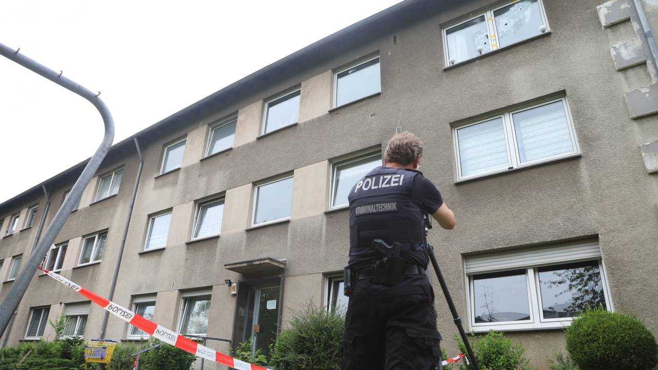 Ein Polizist steht vor einem Mehrfamilienhaus, das mit Flatterband abgesperrt ist.