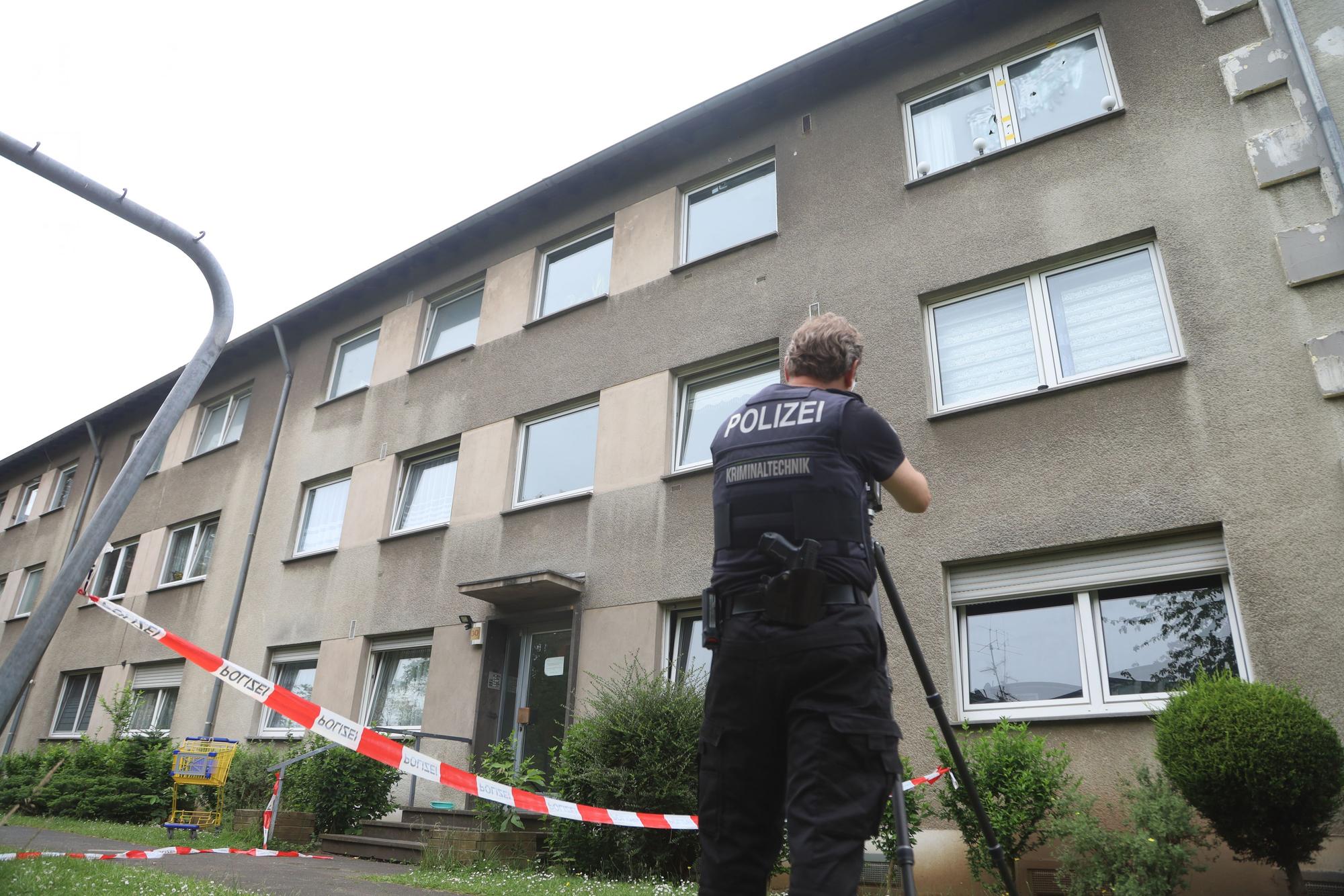 Ein Polizist steht vor einem Mehrfamilienhaus, das mit Flatterband abgesperrt ist.