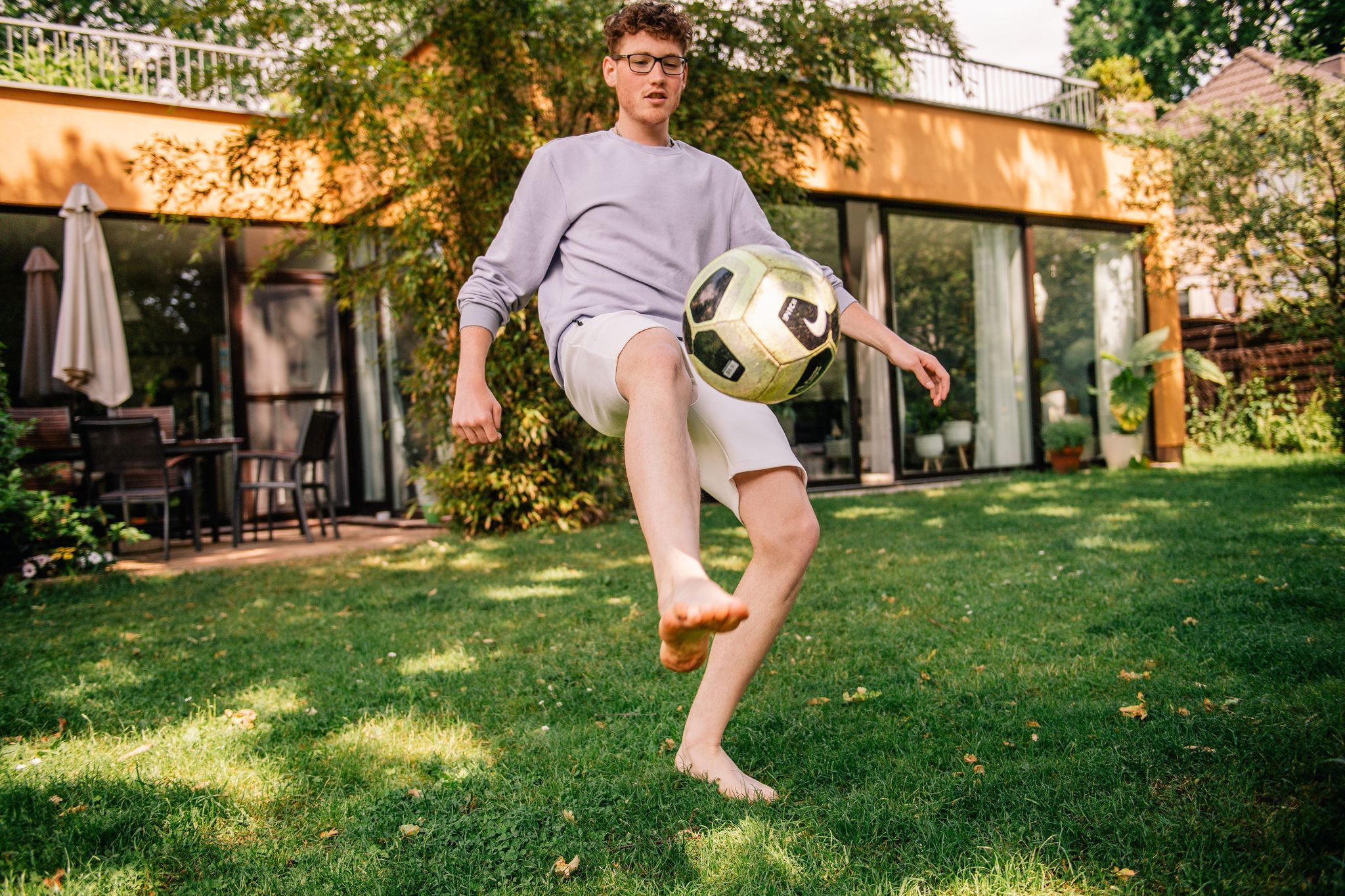 Junger Mann kickt einen Fussball barfüßig im Garten