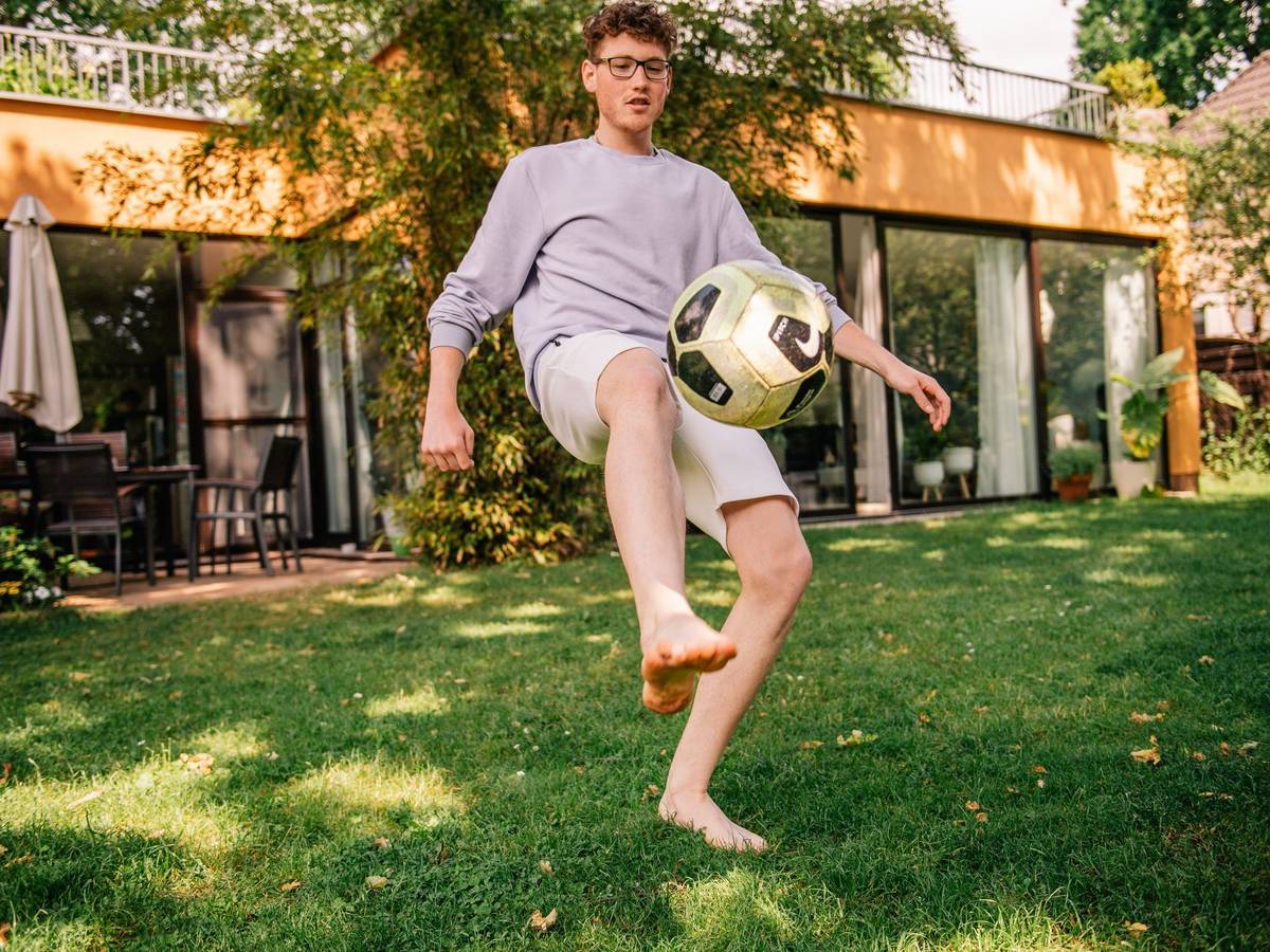 Junger Mann kickt einen Fussball barfüßig im Garten