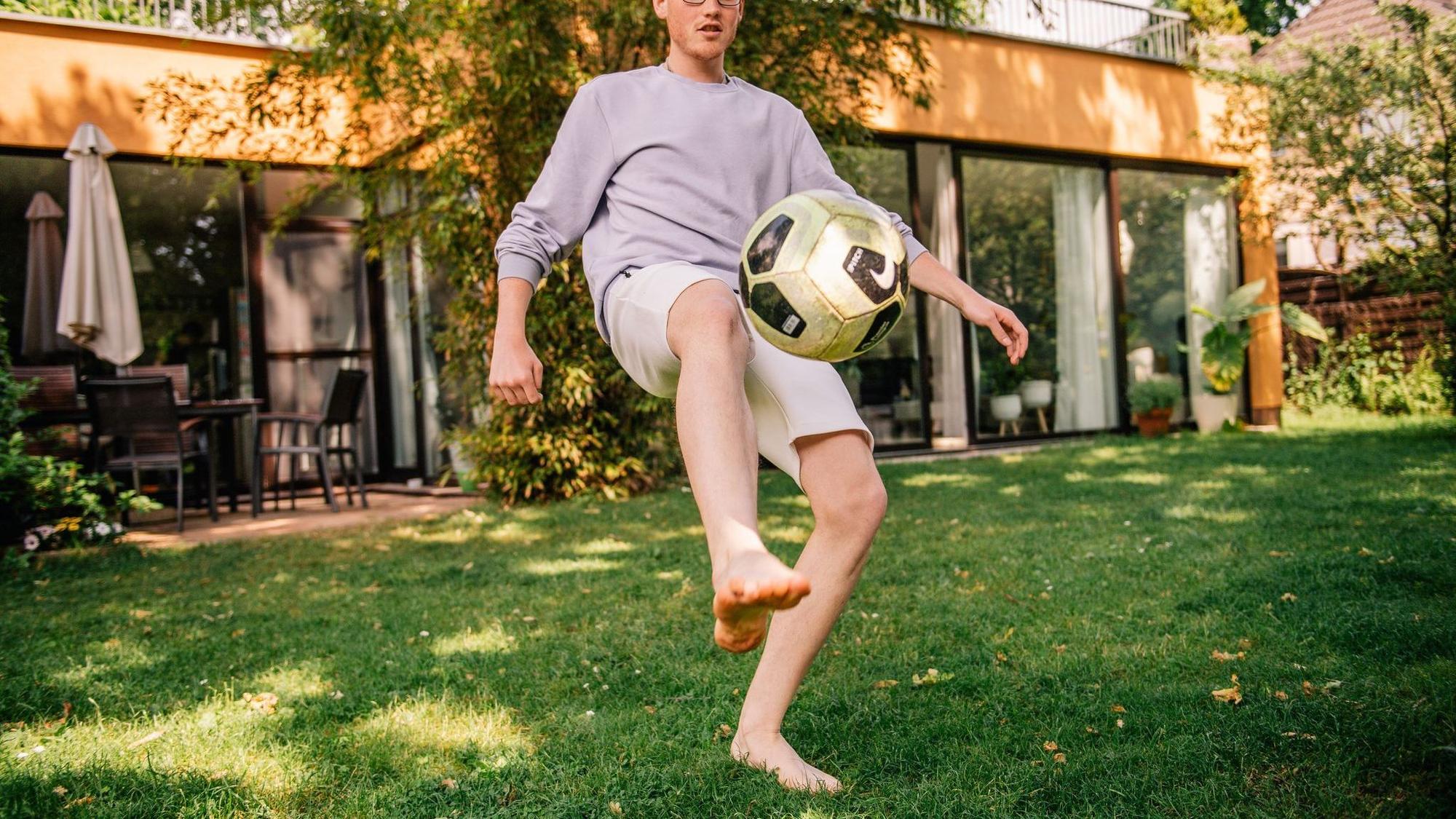 Junger Mann kickt einen Fussball barfüßig im Garten