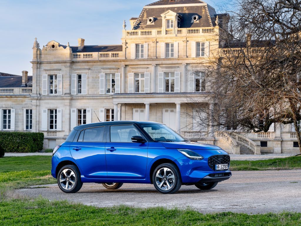 Suzuki Swift 1.2 Club in Blau steht vor einem schönen Anwesen in der Abendsonne.