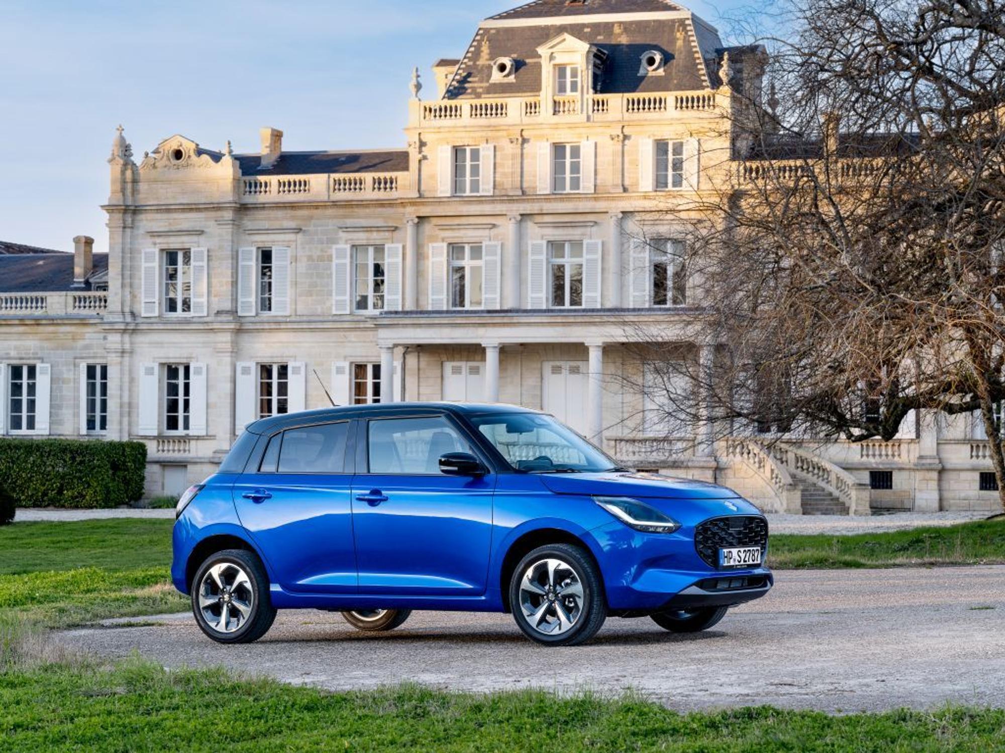 Suzuki Swift 1.2 Club in Blau steht vor einem schönen Anwesen in der Abendsonne.