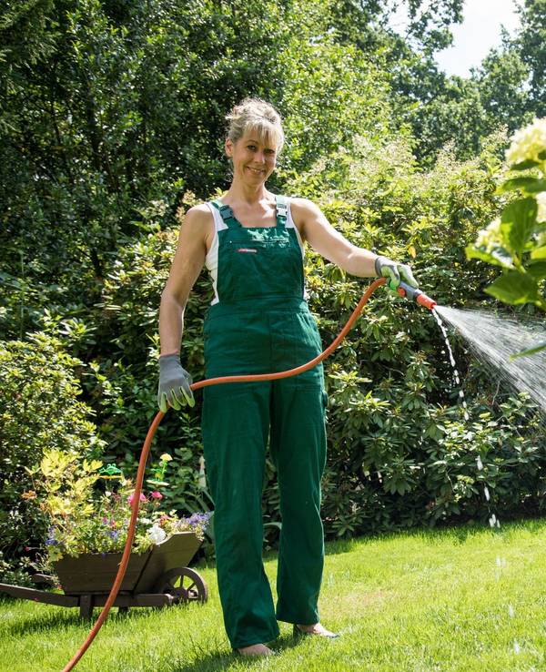 Eine Frau gießt Pflanzen mit einem Gartenschlauch