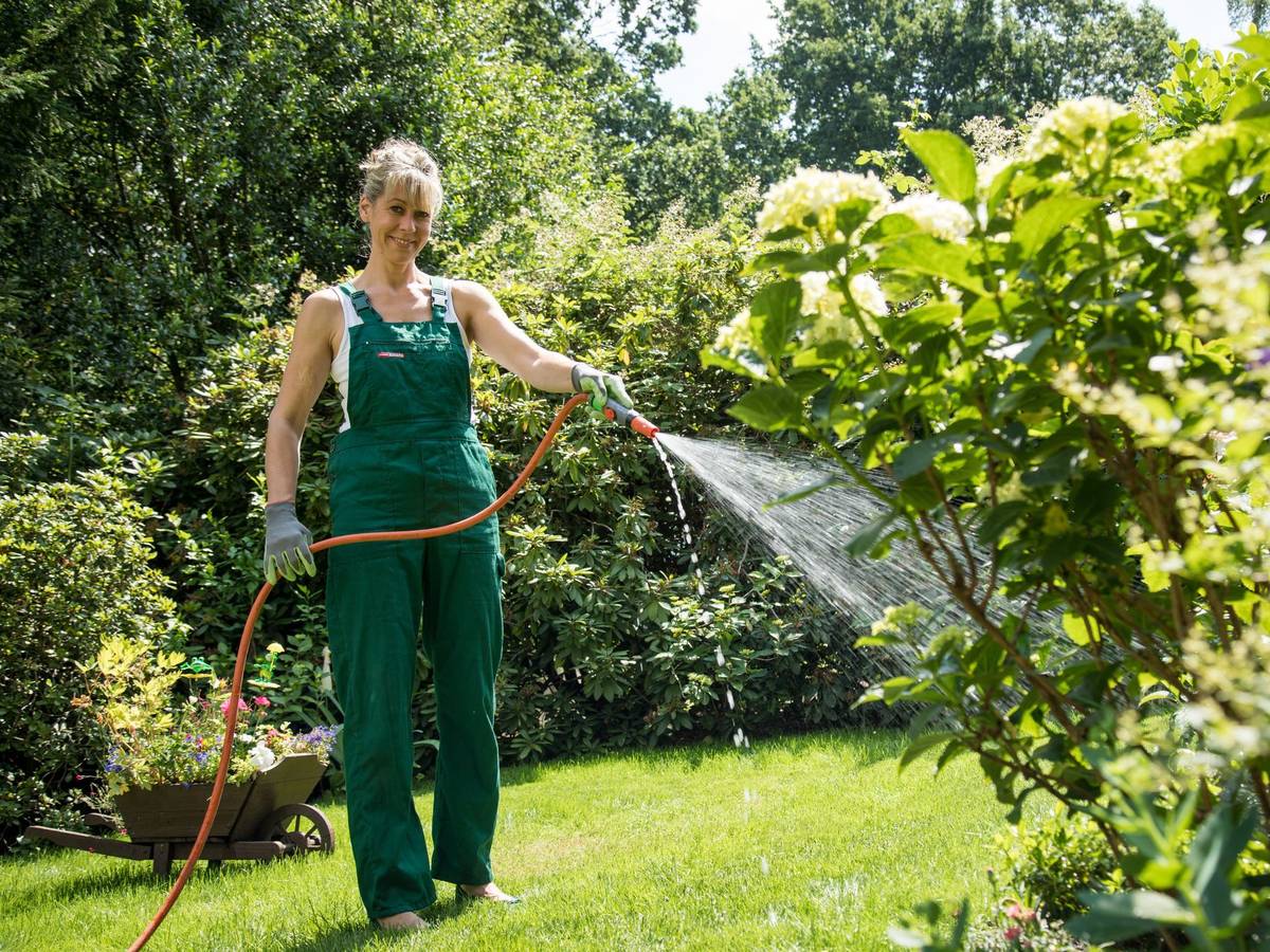 Eine Frau gießt Pflanzen mit einem Gartenschlauch