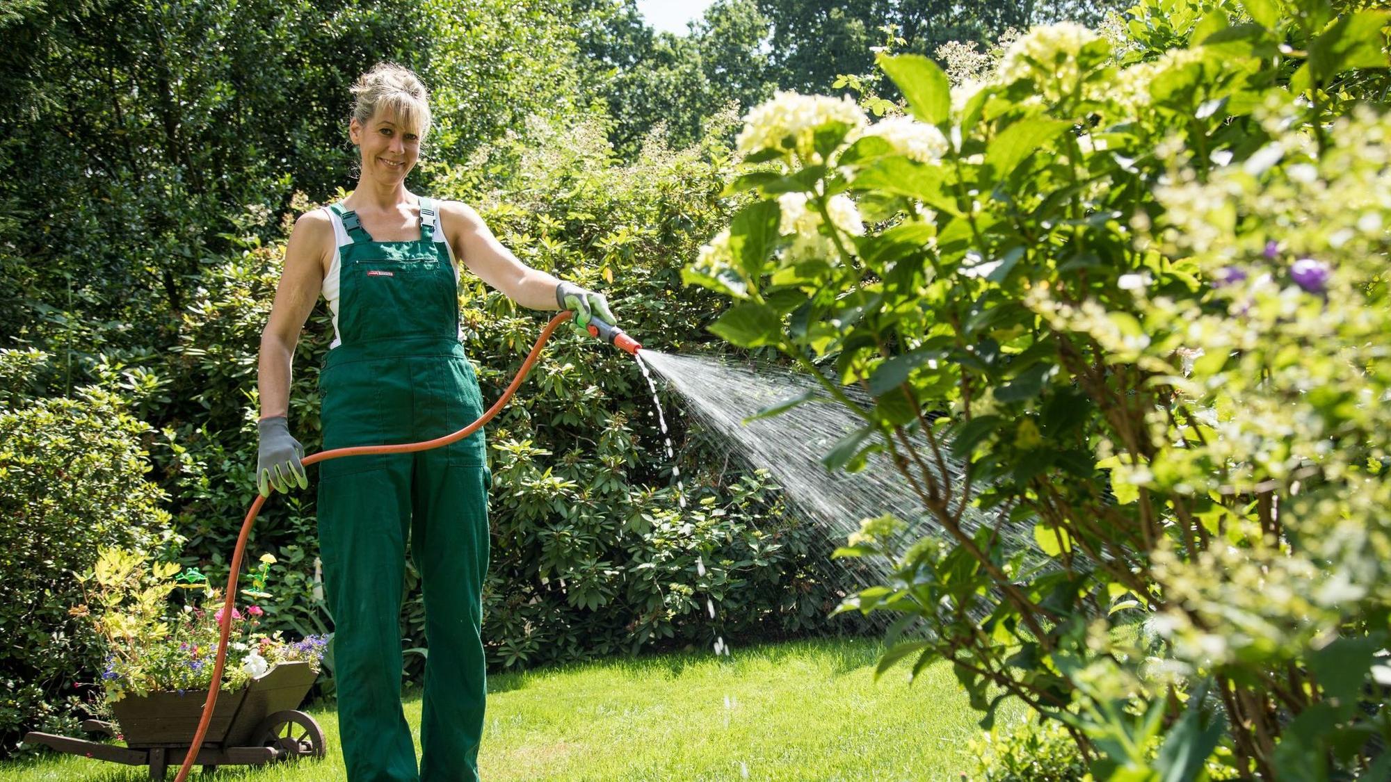 Eine Frau gießt Pflanzen mit einem Gartenschlauch