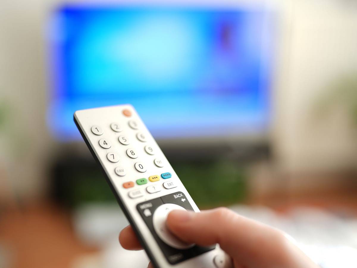 Ein Mann drückt einen Knopf auf einer TV-Fernbedienung