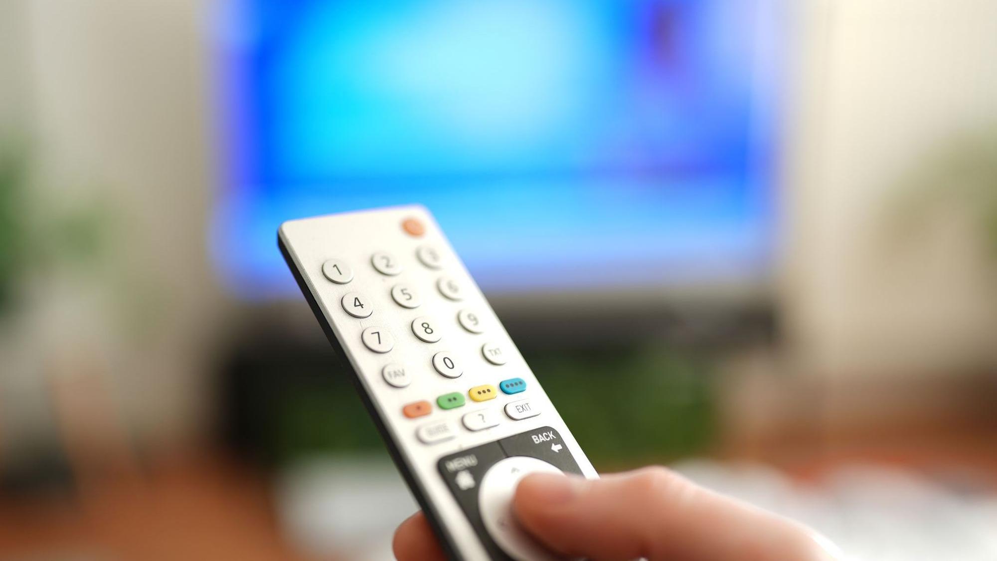 Ein Mann drückt einen Knopf auf einer TV-Fernbedienung