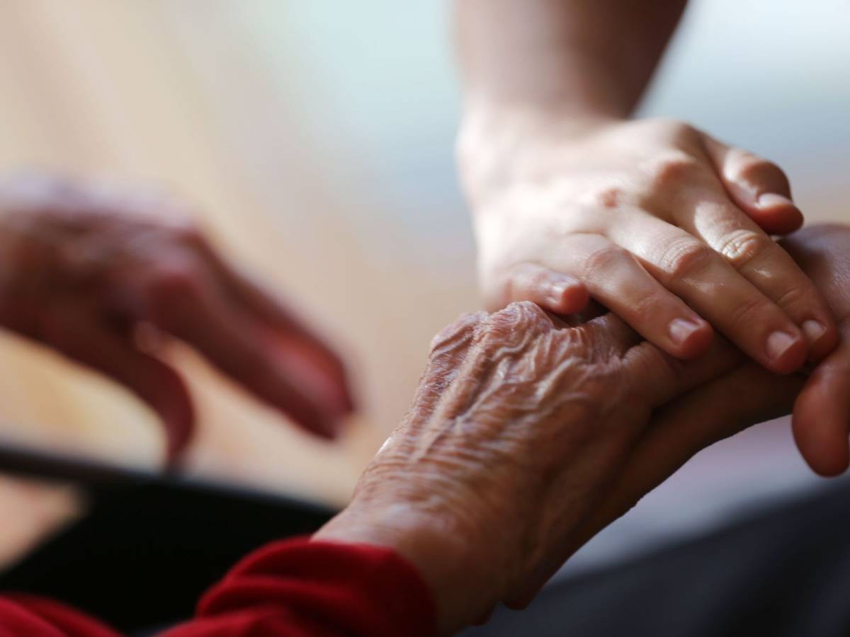 Eine Pflegekraft streicht einer Seniorin über die Hand