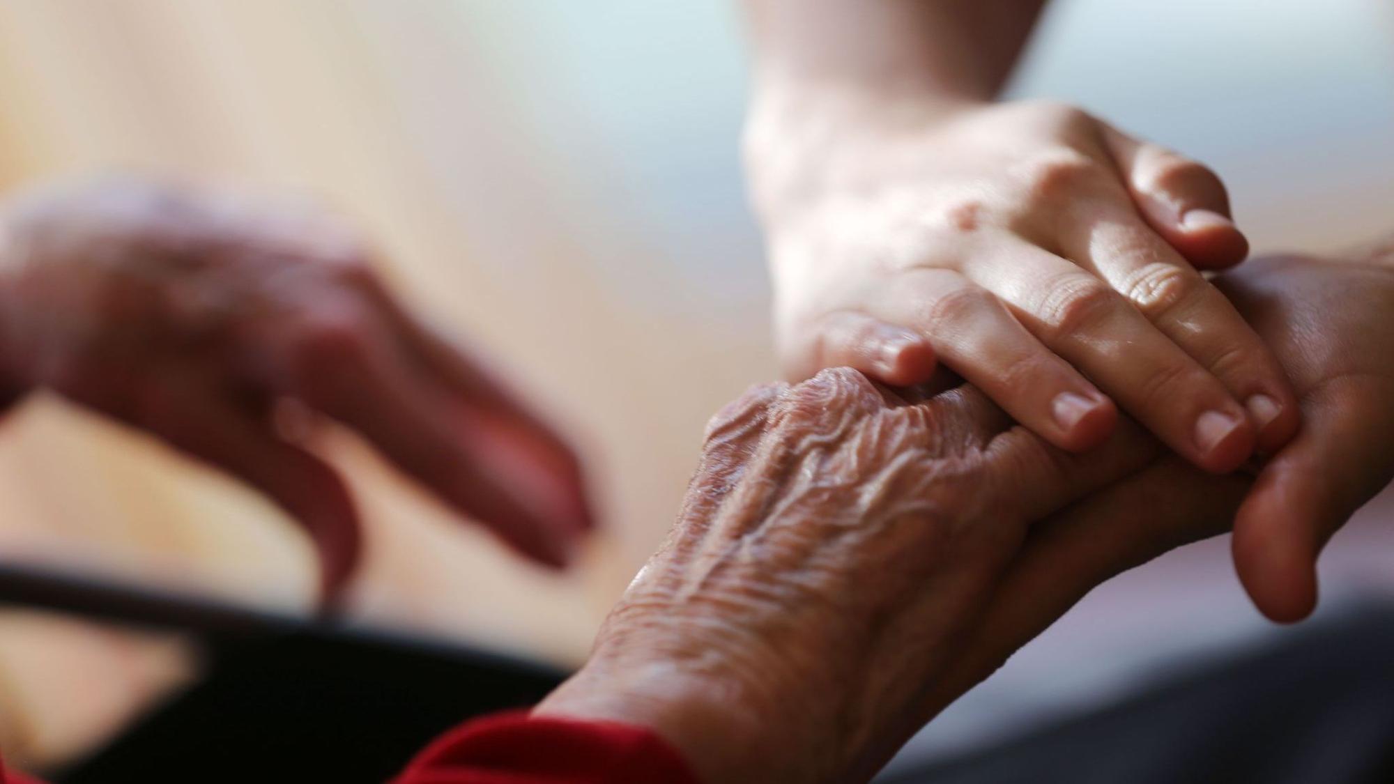 Eine Pflegekraft streicht einer Seniorin über die Hand