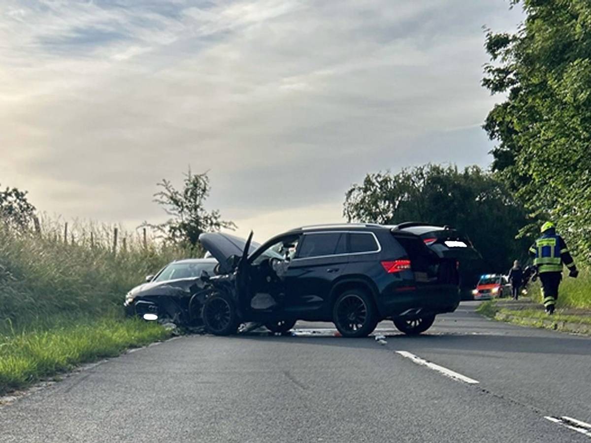 Ein verunfalltes Auto steht am Straßenrand, im Hintergrund ein Polizeiwagen.